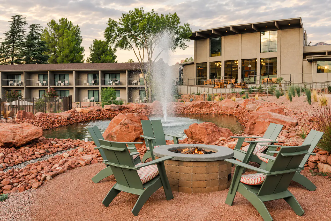 Green Adirondack chairs around a fire pit beside a fountain and red rock boulders in a hotel courtyard in Sedona, Arizona